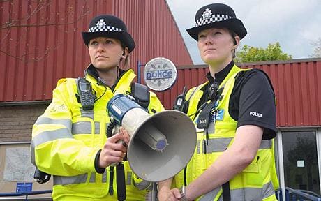Two white police oficers in high vis uniforms stand, One has a megaphone. 