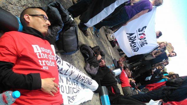 Activists lie in a road, connected to each other by arm tubes, while other protesters stand around them