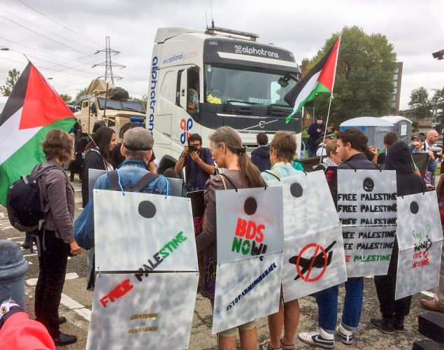 people holding Palestinian flags and wearing sandwich boards made to look like the apartheid wall stand in front of a truck