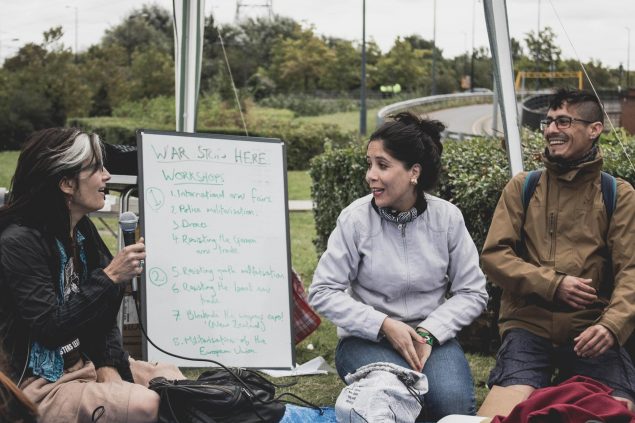 Three campaigners present from a white board showing an event agenda, in an outdoor setting.