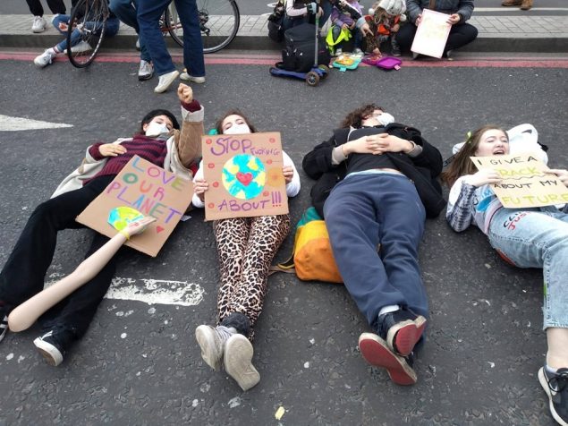 Three activists lying on the ground with placards saying "love our planet" and images of the world surrounded by love hearts.