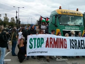 activists block a lorry from entering using a banner reading "stop arming israel"